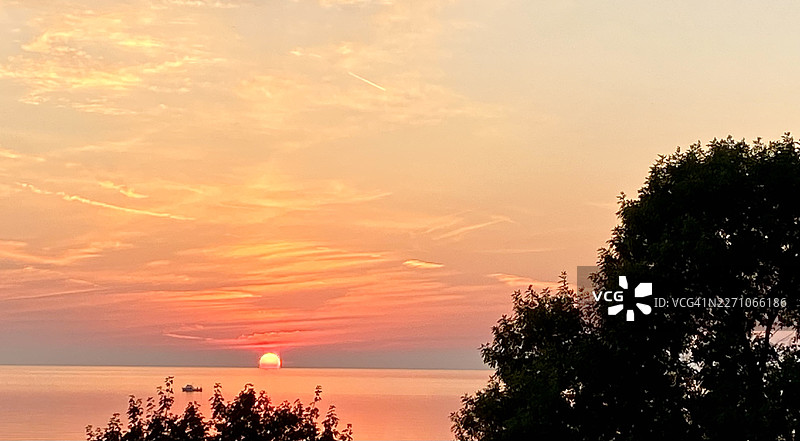 金色的日落映照着大海，远处的树木和船只构成了一幅宁静而风景如画的画面，地点：拉辛，美国图片素材