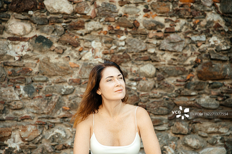 一位女士若有所思地坐在粗糙的石头墙边眺望图片素材