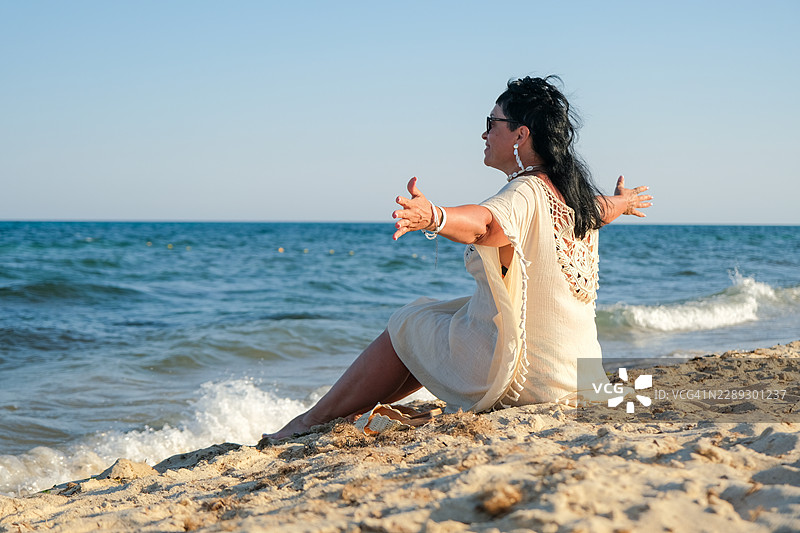 一位女子在阳光明媚的日子里，在突尼斯哈马马特的海滩和海洋边张开双臂，享受宁静。图片素材