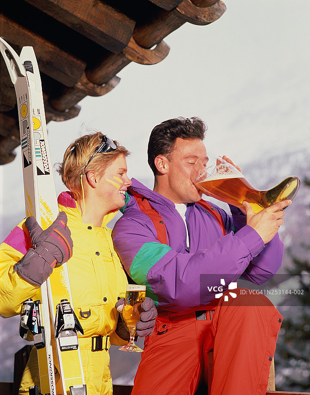 穿着滑雪服，男人从靴子形状的玻璃杯里喝啤酒图片素材