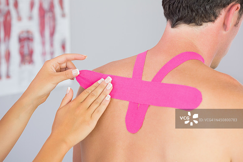 理疗师为男患者背部贴上粉色肌内效贴图片素材
