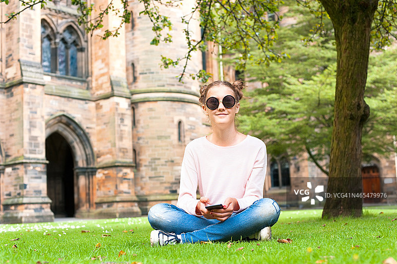 坐在格拉斯哥大学花园里玩手机的年轻女人图片素材