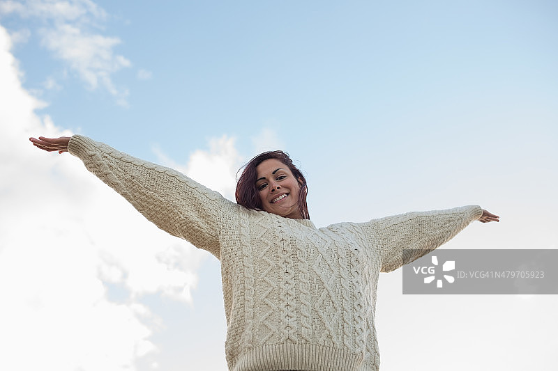 穿着白色毛衣的女人对着天空伸展双臂图片素材