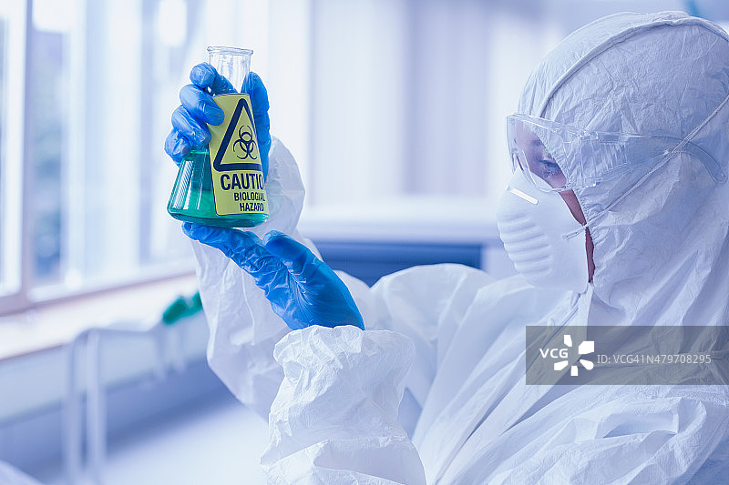 实验室中穿防护服的科学家，手持装有危险化学品的烧瓶图片素材