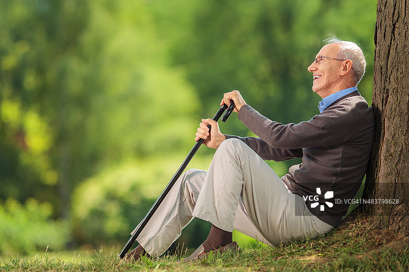 老年绅士拄着拐杖坐在树旁图片素材