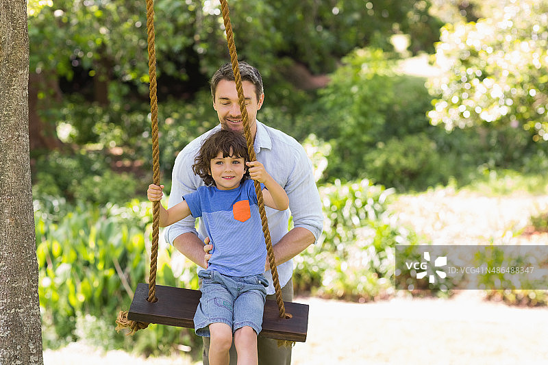快乐的父亲推着男孩荡秋千图片素材