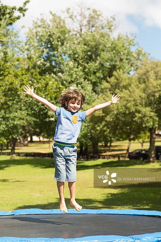 在公园蹦床上跳高的快乐男孩图片素材
