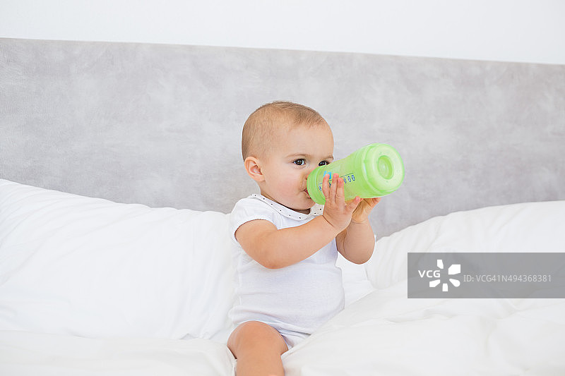 抱着奶瓶的可爱宝宝坐在床上图片素材