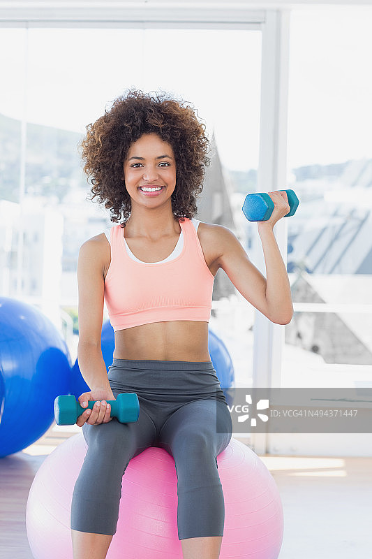 女人在健身球上用哑铃锻炼图片素材