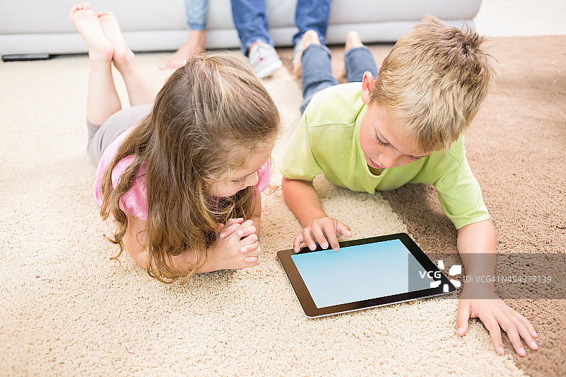笑容满面的兄妹在地毯上使用平板电脑图片素材