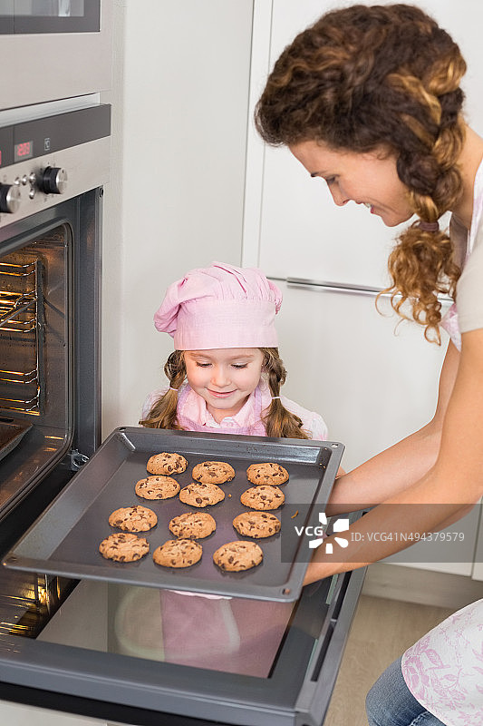 母亲从烤箱里拿出饼干，小女孩在一旁观看图片素材