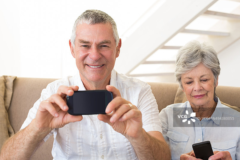 老年夫妇坐在沙发上使用智能手机图片素材