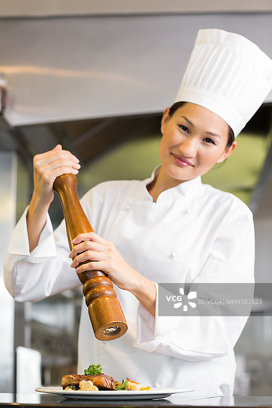微笑的女厨师在厨房研磨食物上的胡椒粉图片素材