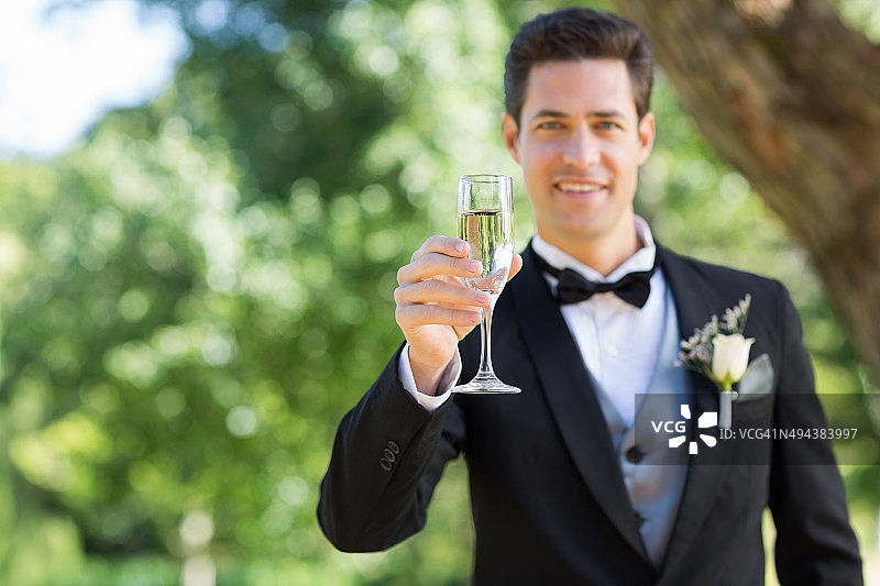 笑容满面的新郎在花园里拿着香槟酒杯图片素材
