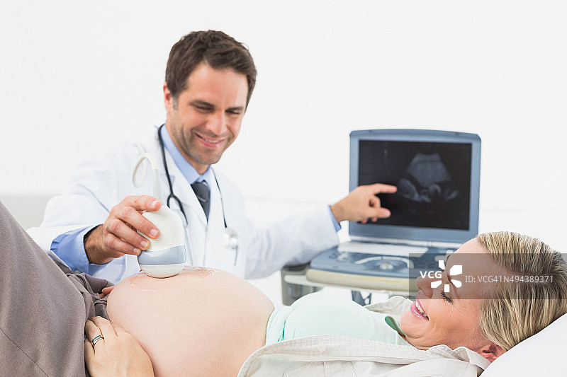 快乐的医生在超声波检查中向金发孕妇展示她的宝宝图片素材