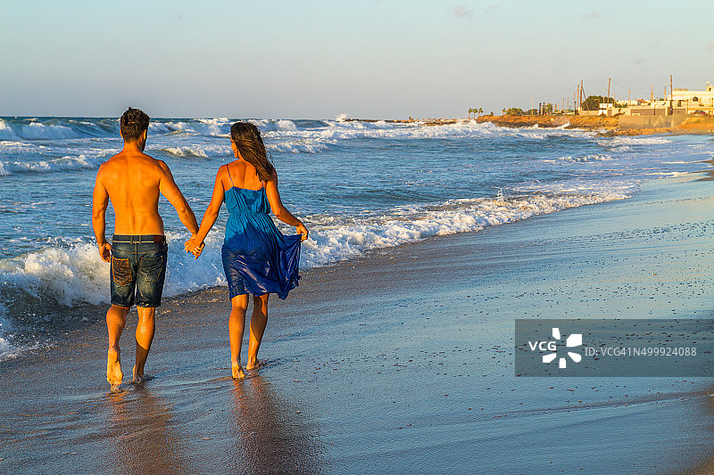 一对年轻夫妇在黄昏时分赤脚走在湿润的沙滩上图片素材