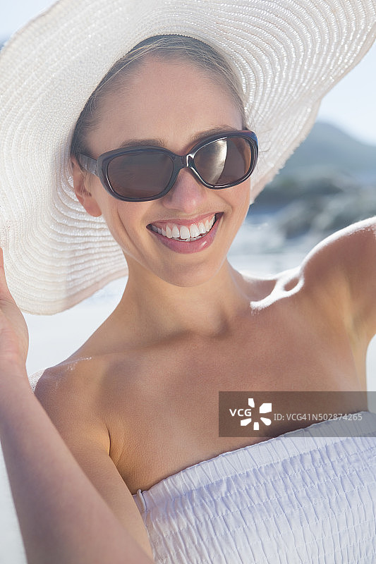 在海滩上戴着遮阳帽，身穿白色连衣裙的金发女子图片素材