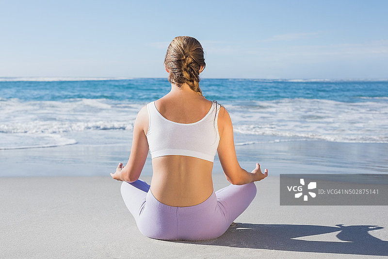 在海滩上以莲花坐姿势坐着的运动型金发女郎图片素材