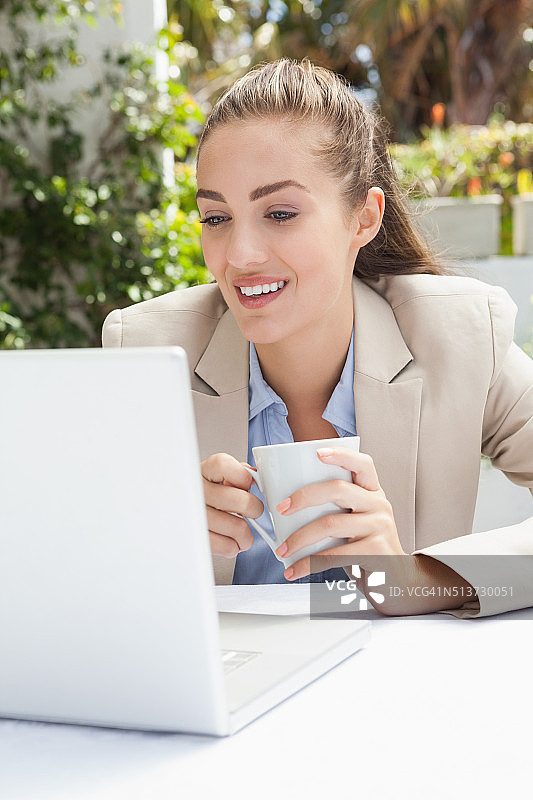 使用笔记本电脑喝咖啡的漂亮女商人图片素材