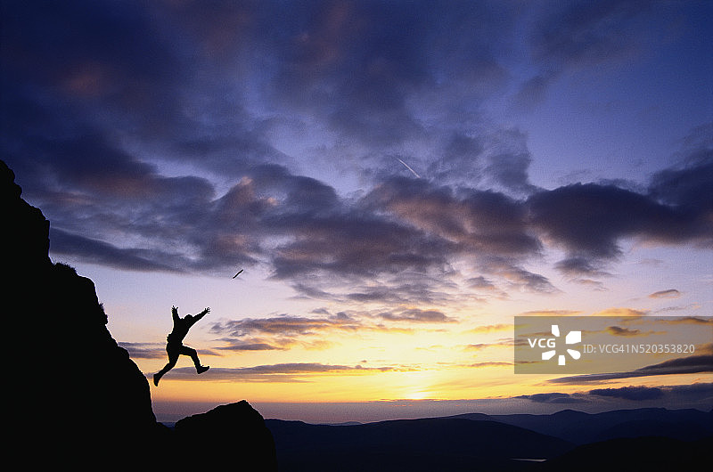 登山者在日落时分从岩石上跳跃图片素材