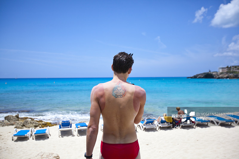 在海滩上使用智能手机的晒伤纹身男子图片素材