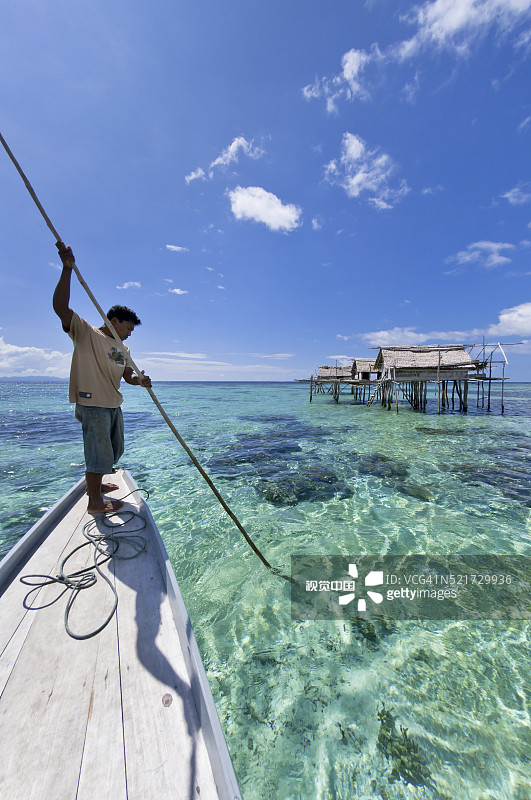 男人在托吉安岛清澈的海水中用矛在木船上钓鱼图片素材