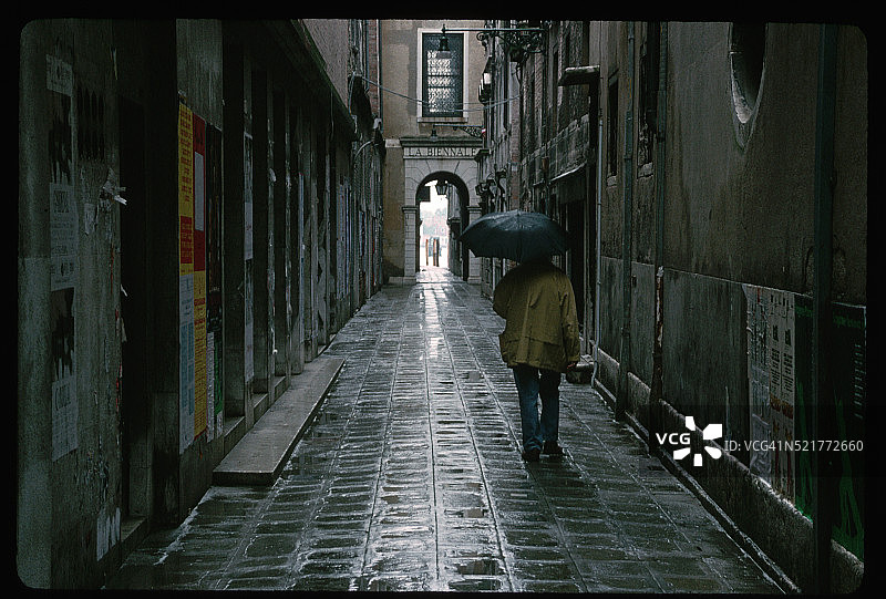 打着伞走在潮湿小巷里的男人图片素材