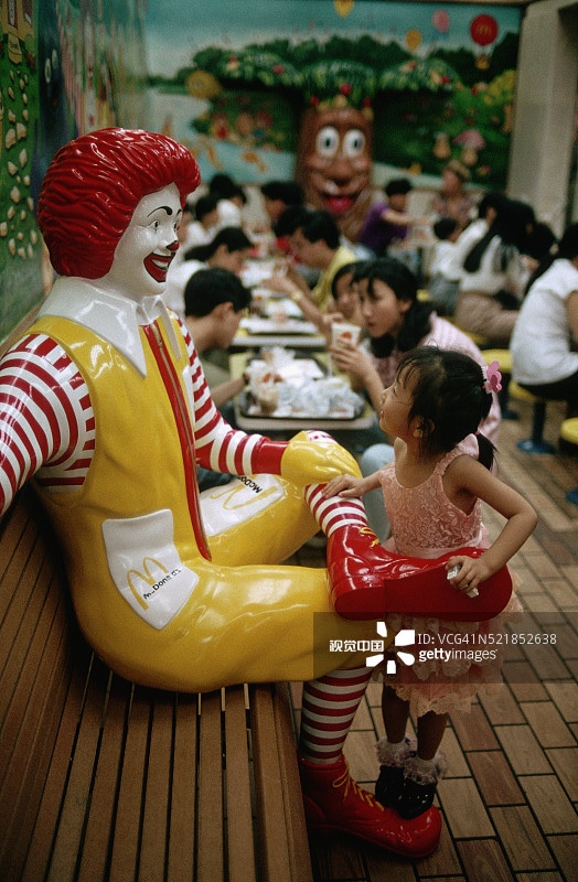 在麦当劳叔叔雕像上玩耍的女孩图片素材