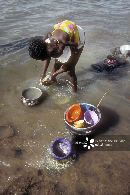 抱着妹妹的年轻西非女孩在洗碗图片素材