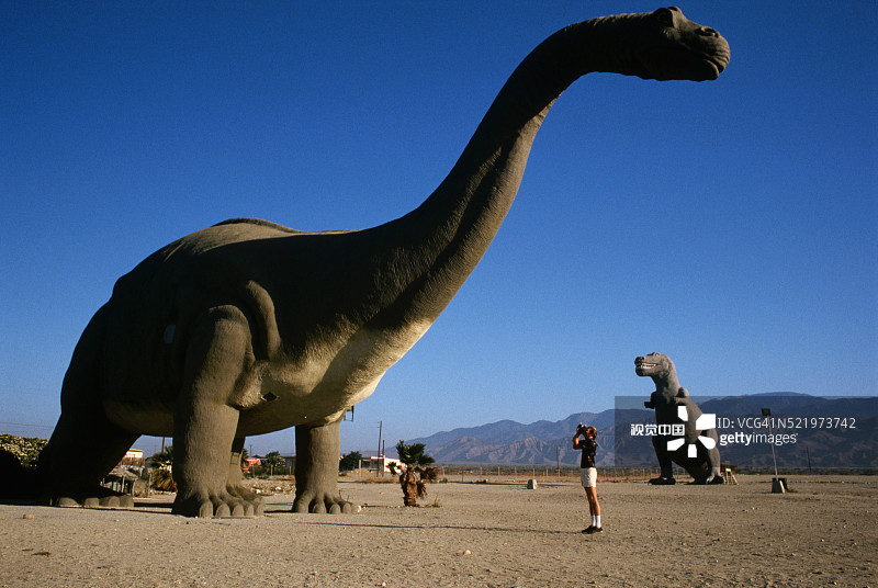 与恐龙雕像合影的游客图片素材