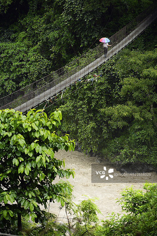 在尼泊尔安纳布尔纳峰环线布尔布勒村拉姆琼区悬索桥上撑伞的男人图片素材