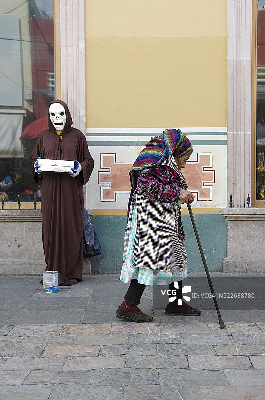 墨西哥阿瓜斯卡连特斯，戴骷髅面具的男人身旁走过的年长女性图片素材