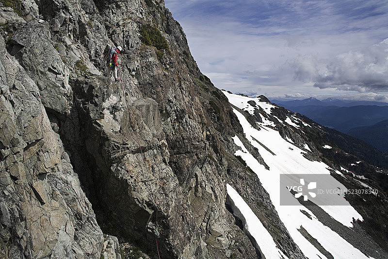 身穿红色夹克的男子在陡峭的悬崖上攀岩图片素材