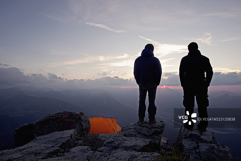 两名年轻男子站在阿尔卑斯山蒂罗尔州帐篷附近较高的岩石上图片素材