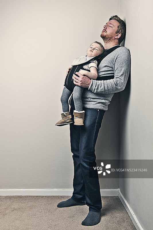 父亲靠在墙上睡着了，婴儿在背带里图片素材