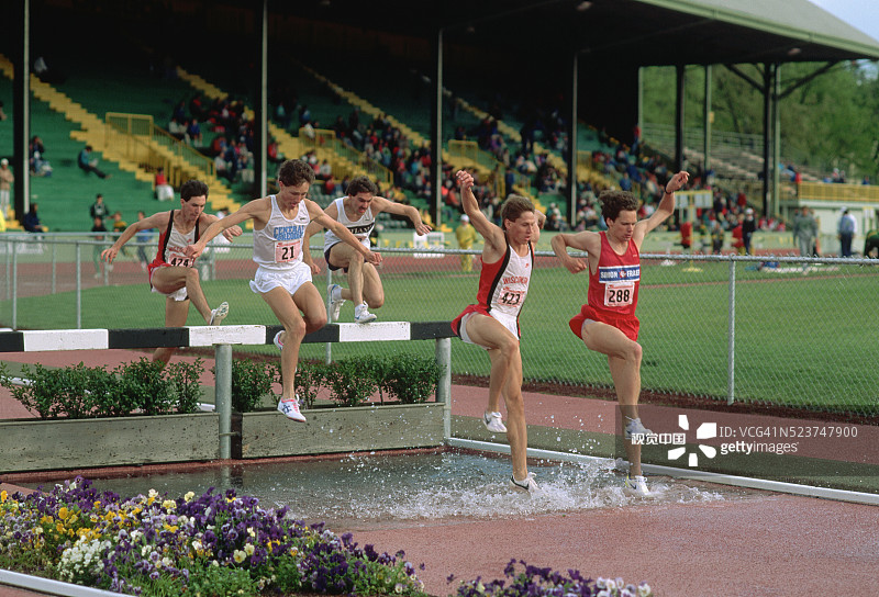跨栏赛跑中跨越水障碍的跑步者图片素材