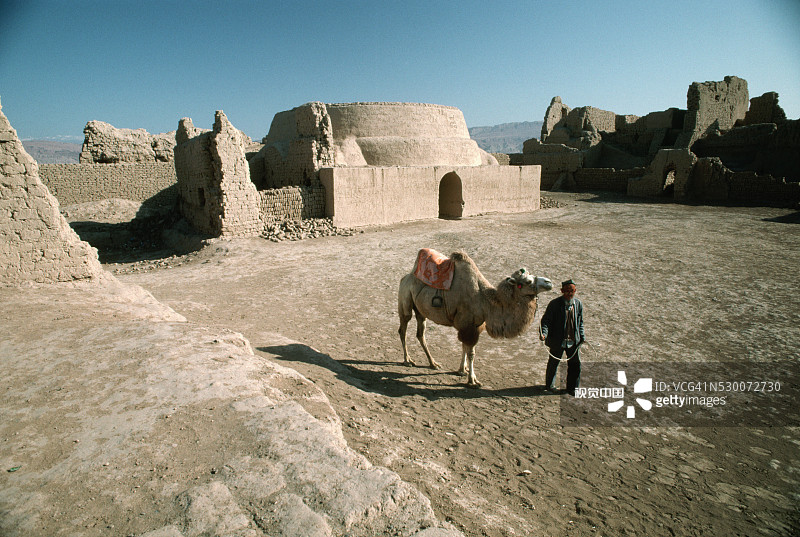 男人在吐鲁番带领骆驼经过废墟图片素材