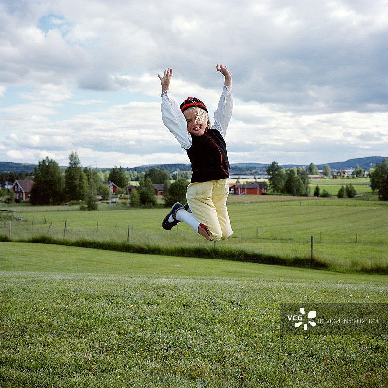 穿着传统服装在草地上跳跃的女孩图片素材