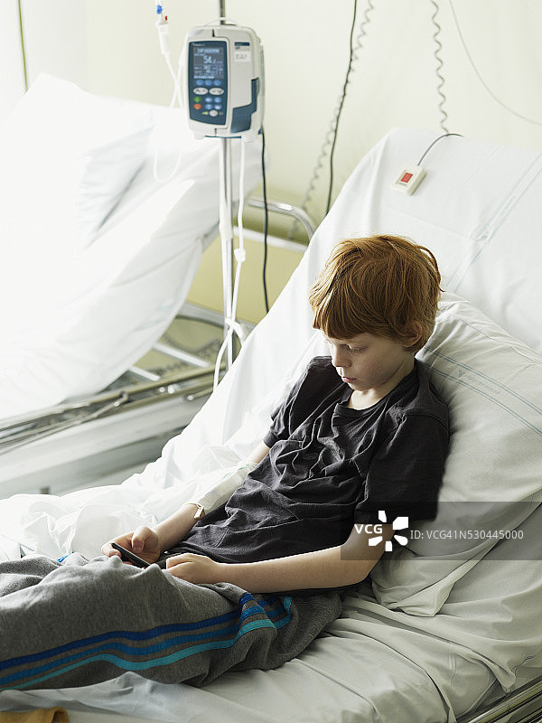 男孩坐在病床上发短信图片素材