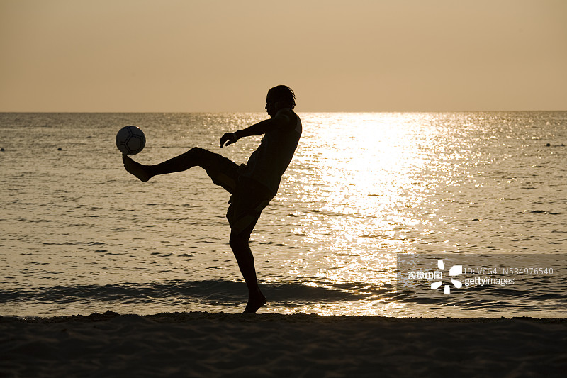 男人在沙滩上踢足球图片素材