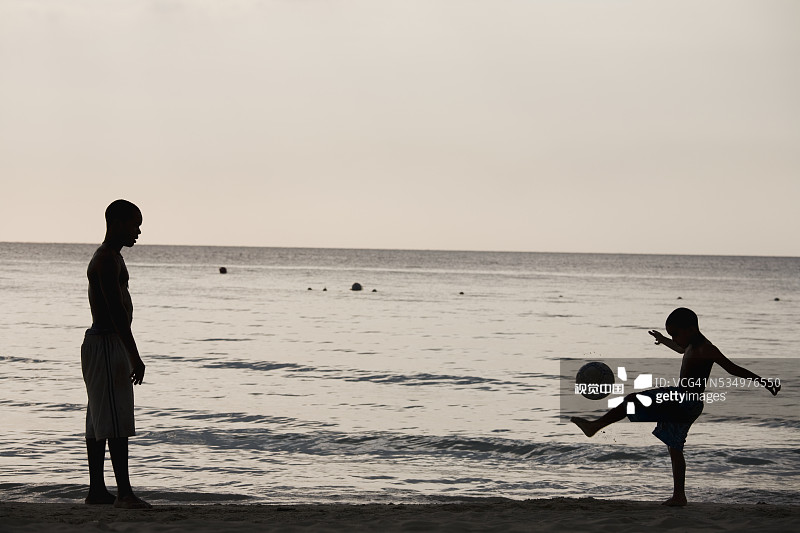 男人和男孩在海滩上踢足球图片素材