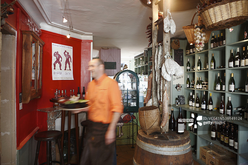 在维朗德里一家餐厅里，穿着橙色衬衫端着托盘的男服务员图片素材