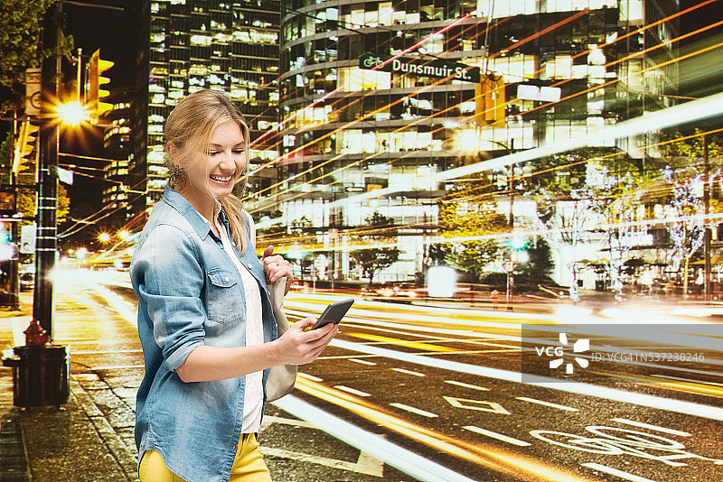 夜晚在城市中使用手机的微笑女人图片素材