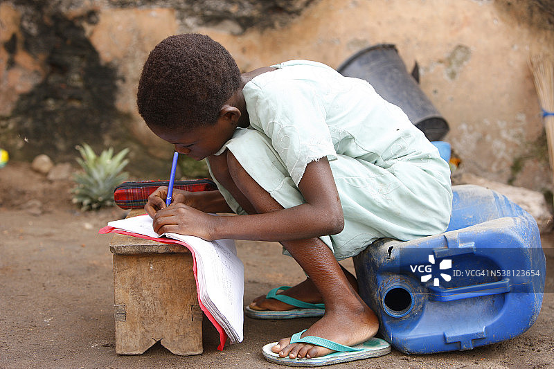 多哥男孩坐在罐子上在凳子上做作业图片素材