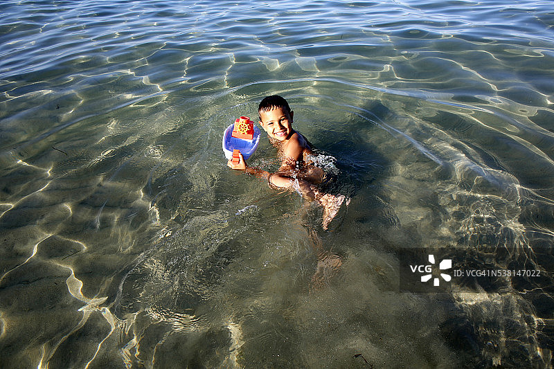 6岁男孩在海边玩玩具船图片素材