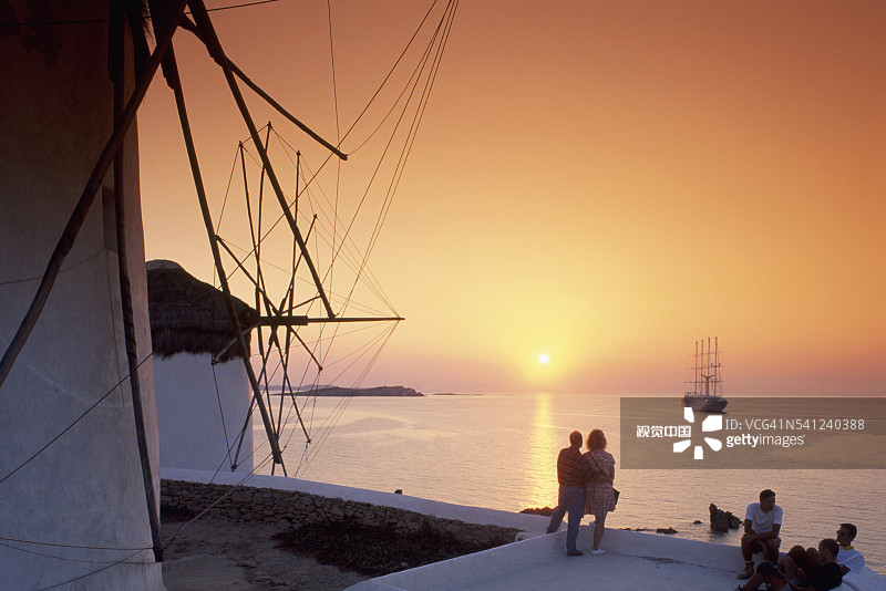 情侣在米科诺斯岛风车旁欣赏日落图片素材
