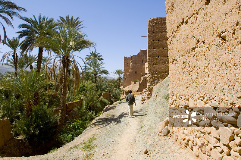 男子在村庄围墙边的小路上行走图片素材