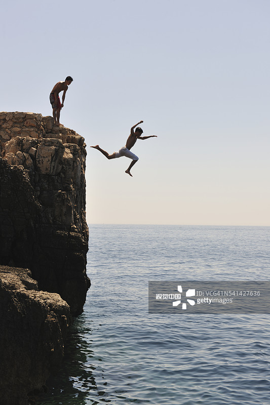 年轻男人从悬崖跳入大海图片素材