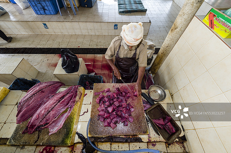 一位商贩在鱼市场将金枪鱼的粉红色鱼肉切成块出售。图片素材