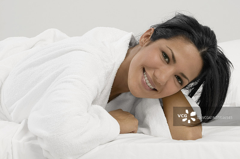 穿着浴袍躺在床上的微笑年轻女人肖像图片素材